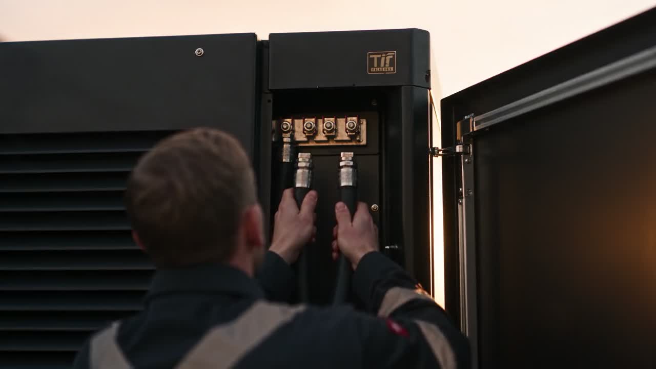 Technician connecting cabling inside a commercial battery storage cabinet at sunset